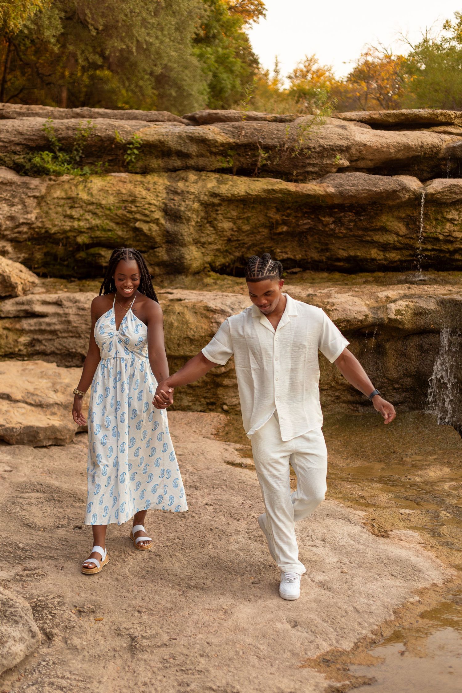 Couple in white outfits dancing together on a rocky terrain during golden hour.
