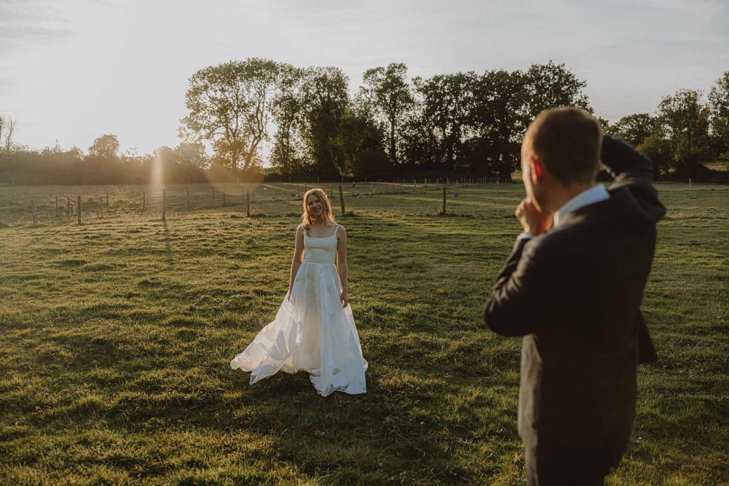 A couple walks hand in hand through a sunlit meadow during golden hour as their wedding day comes to a close.