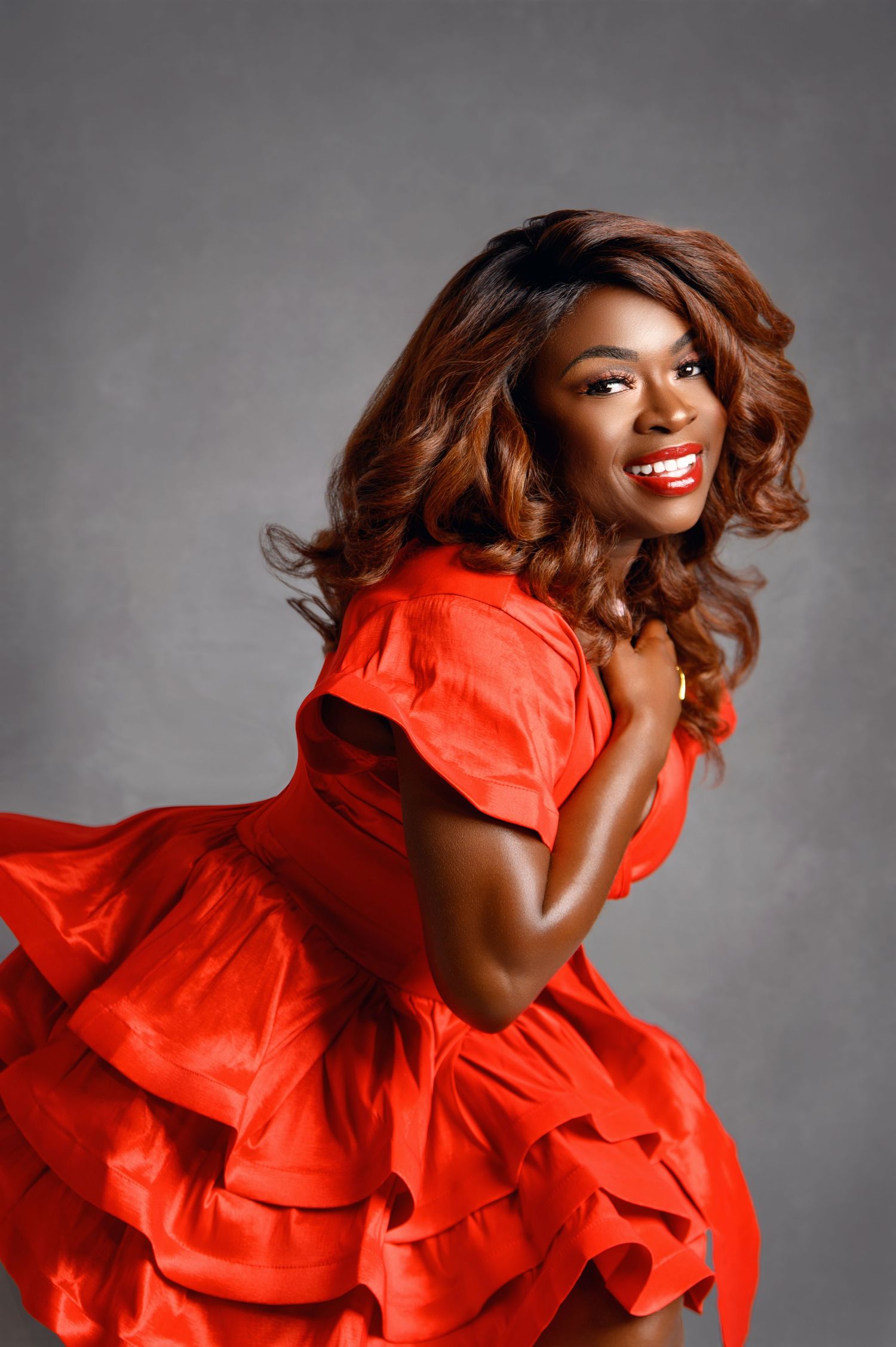 Dynamic fashion shoot featuring flowing red ruffled dress against grey background.