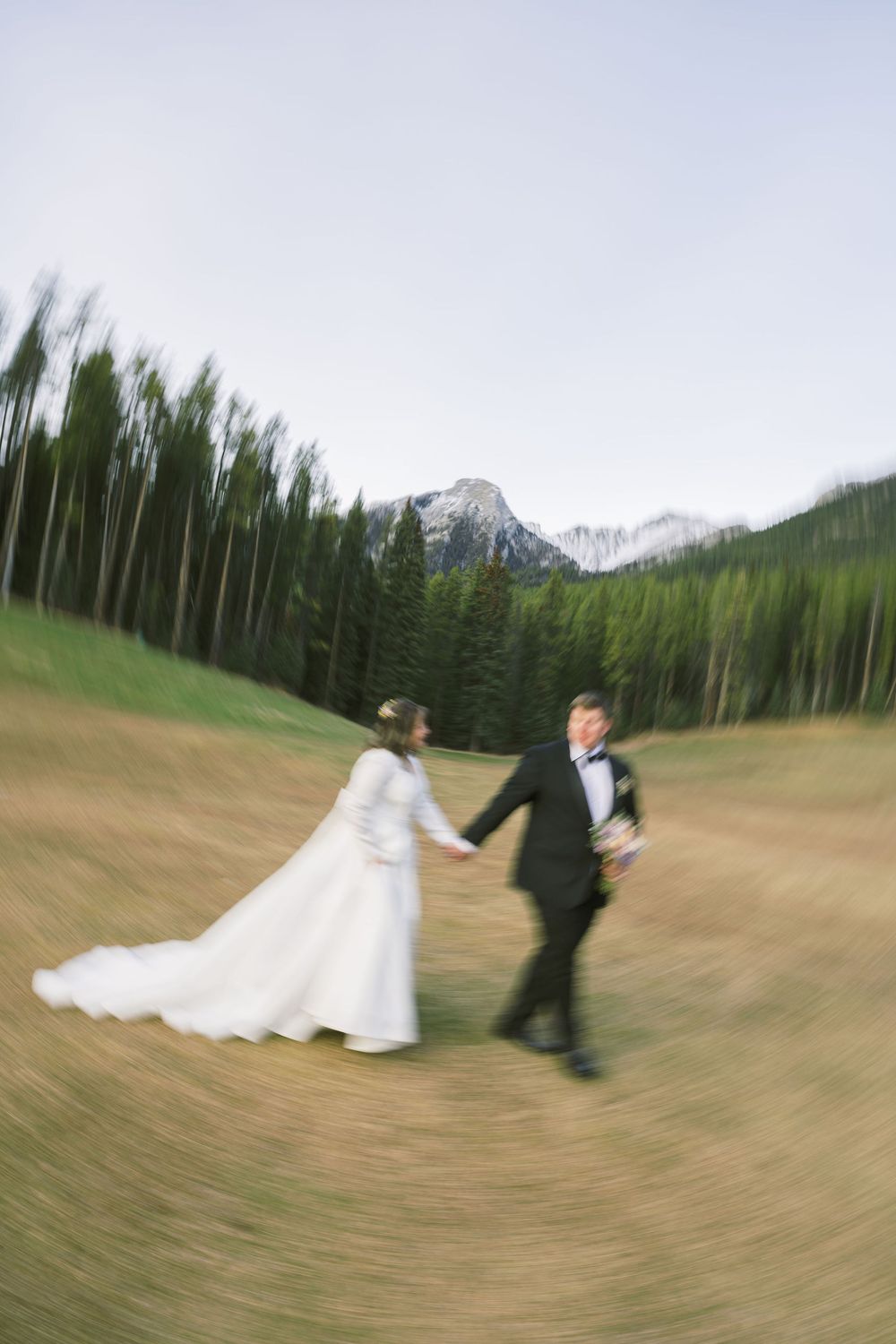 A wedding couple spins in circles creating a blurred motion effect against a mountain landscape backdrop.