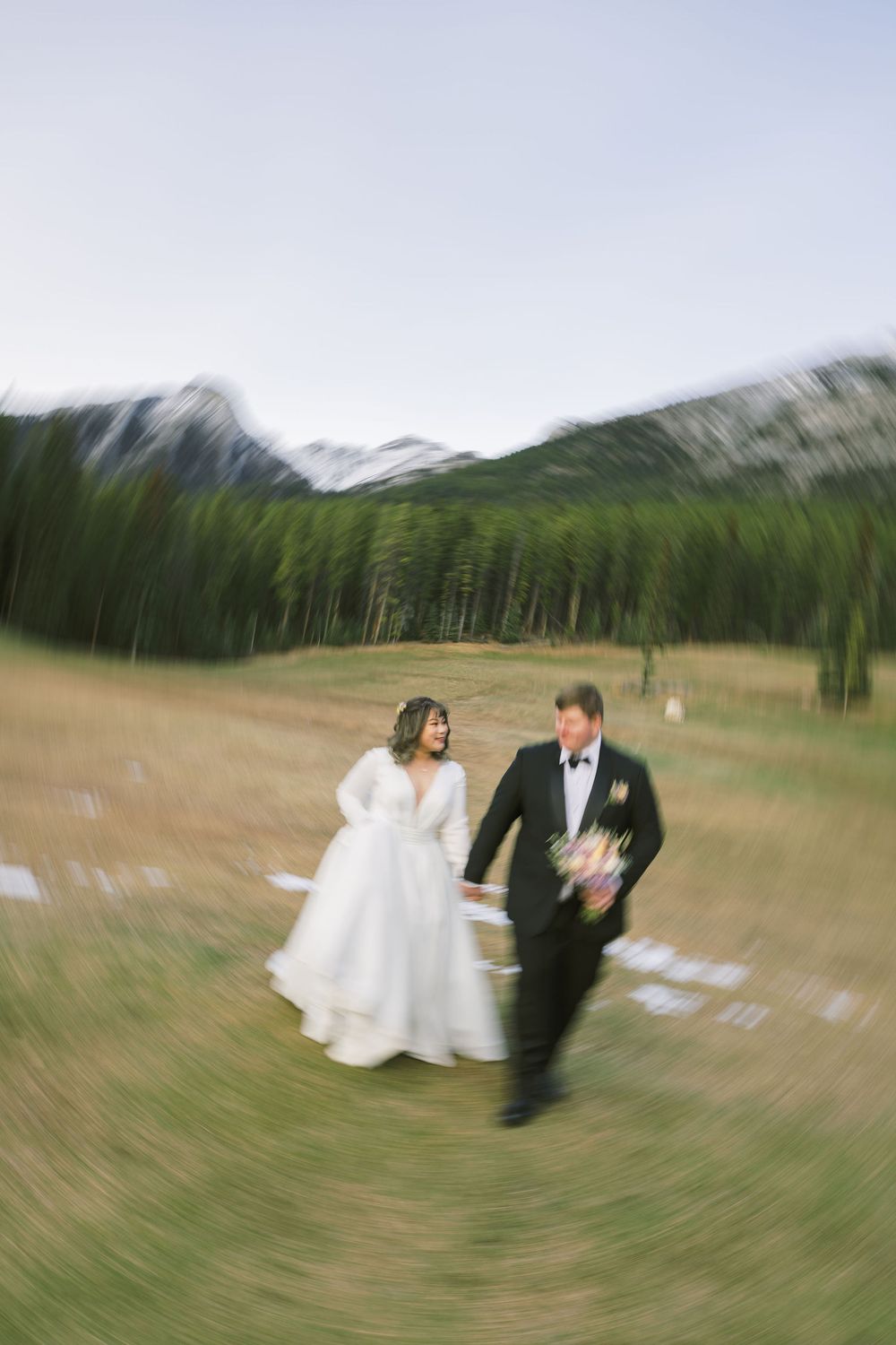 Motion blur photo sequence shows a couple in wedding attire walking across a grassy field with trees in background.