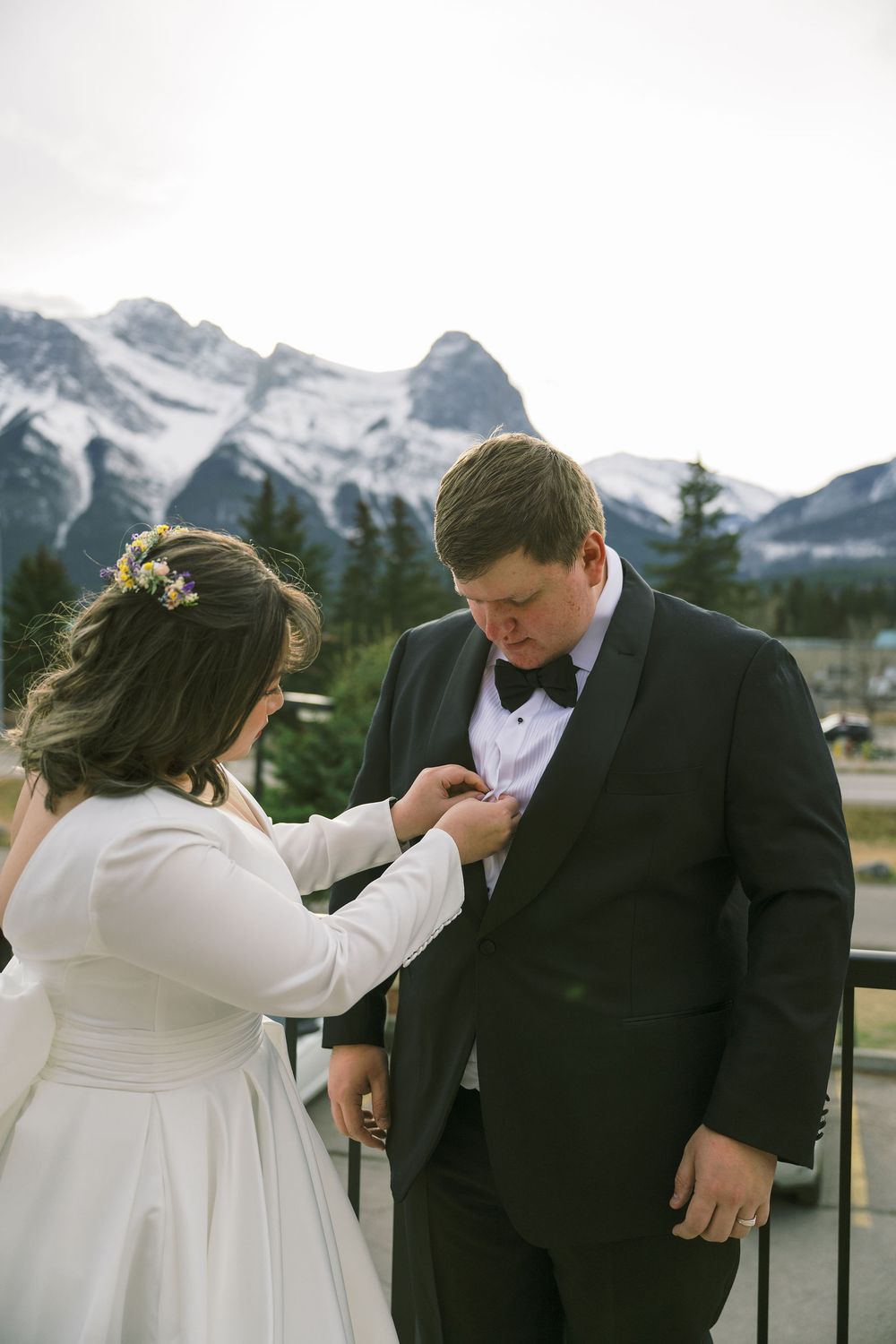 A couple shares an intimate moment outdoors with snow-capped mountain peaks visible in the background.