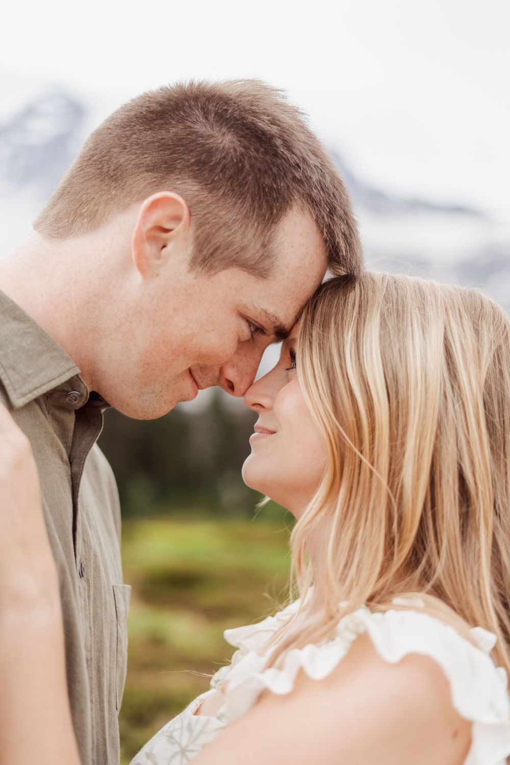 An intimate close-up moment between a couple against a blurred mountain landscape background.