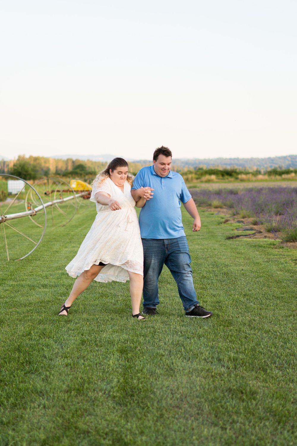 A playful couple poses together on green grass in a field during a summer photoshoot.