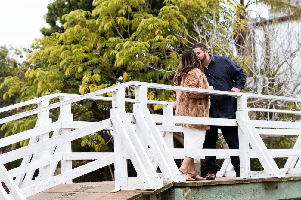 A couple shares a romantic moment on a white wooden bridge surrounded by lush greenery.