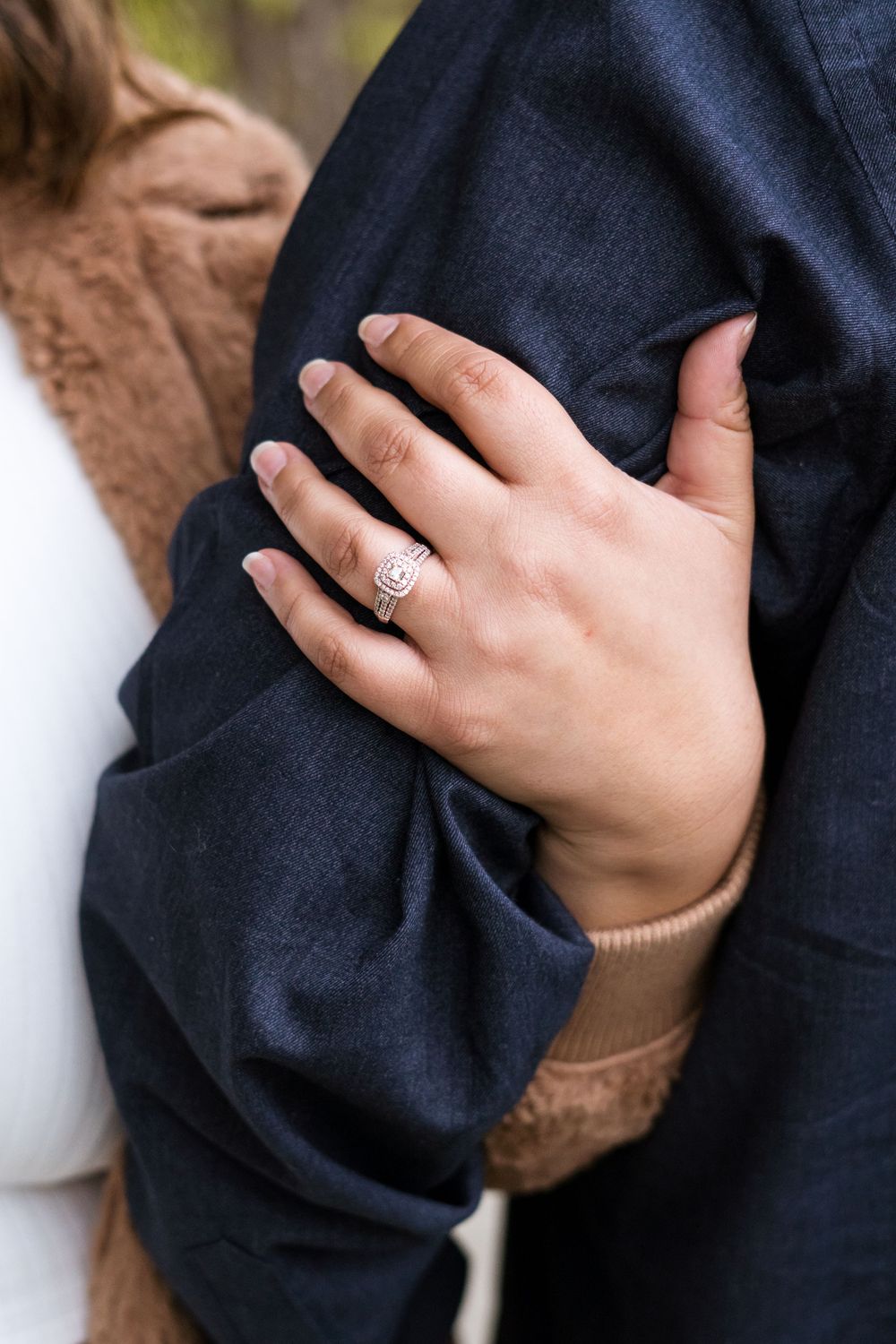 A close-up view of hands wearing a navy blue sweater and a diamond engagement ring.