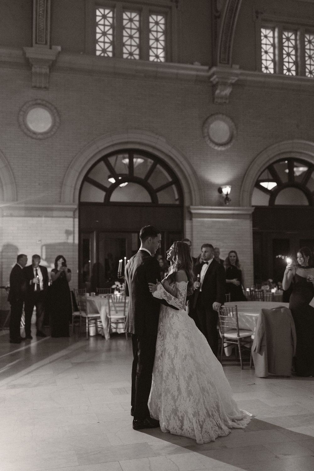 Elegant ballroom wedding venue with couples dancing across a grand marble floor under ornate architecture.