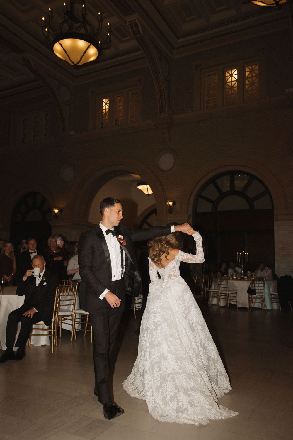 Couples dancing in an elegant ballroom with ornate lighting and decor.