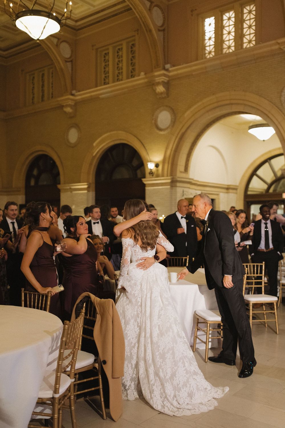 Wedding reception in a grand ballroom with guests dancing and mingling.