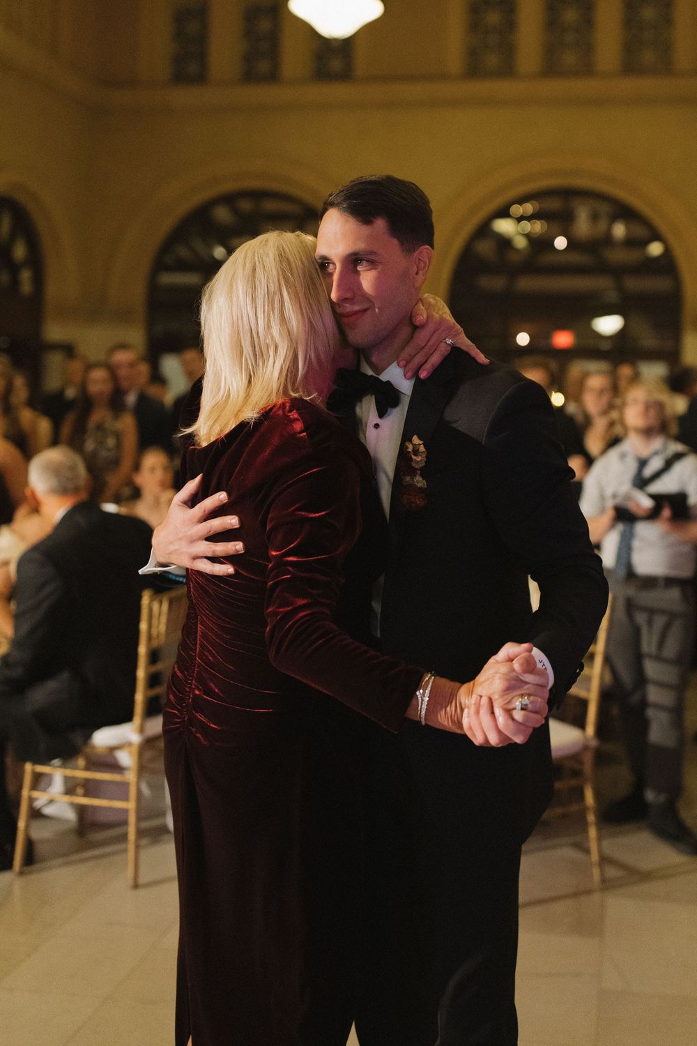 Couples slow dancing in formal attire at an elegant venue with warm lighting.