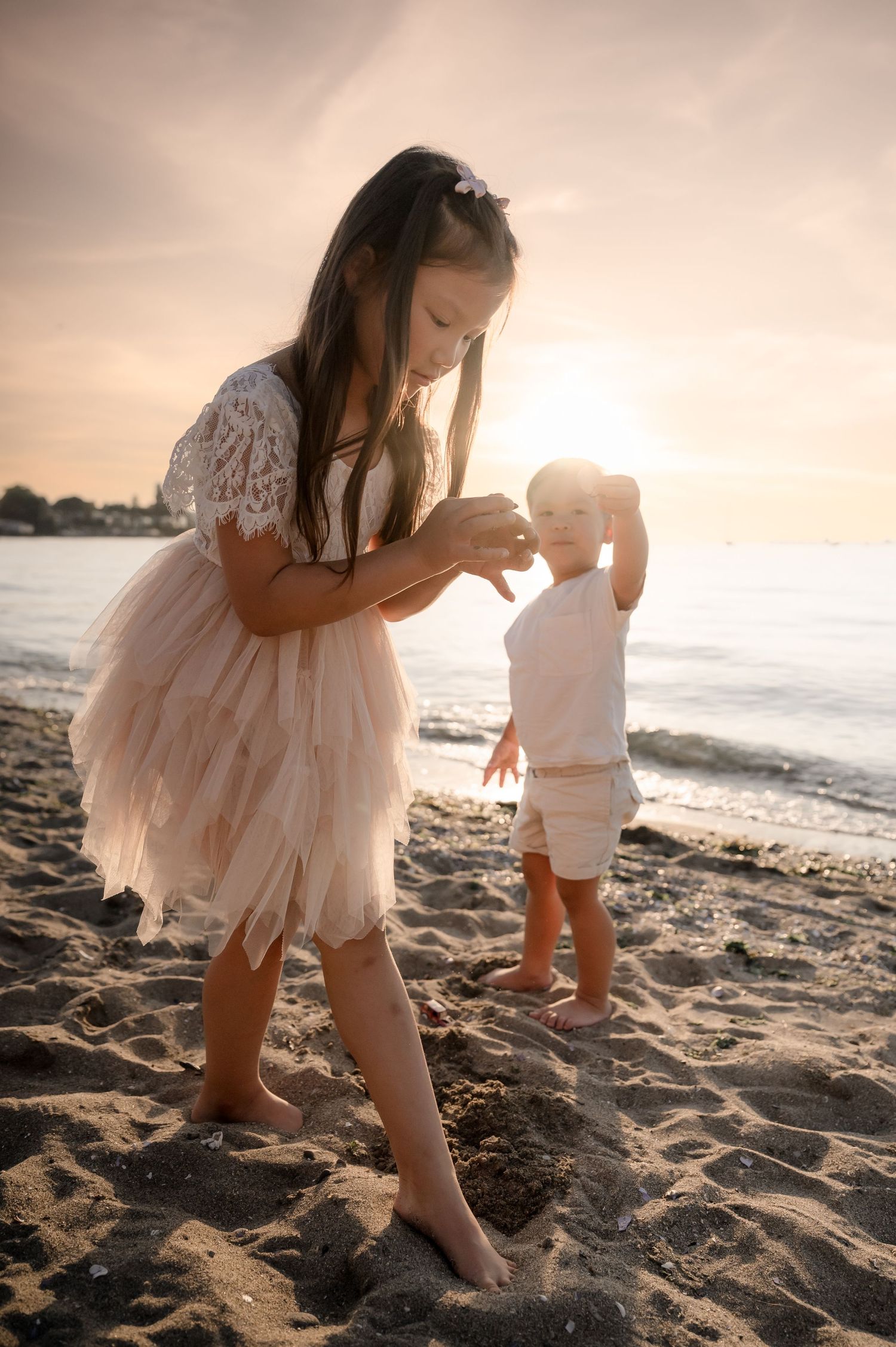 Two figures in white outfits explore a sandy beach at sunset, creating dreamy silhouettes against the golden light.