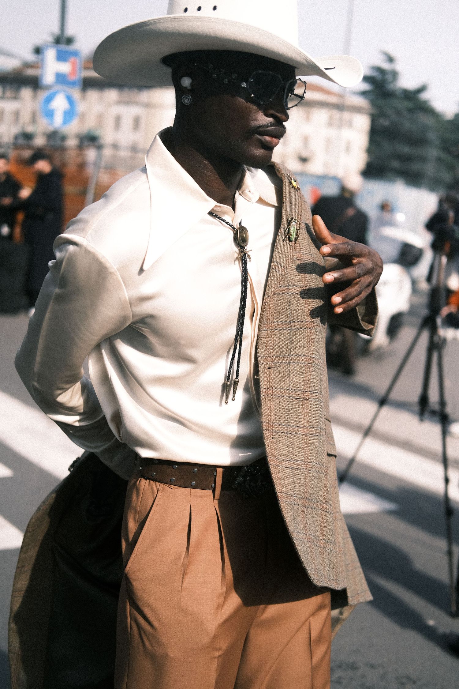 Stylish person in a white turtleneck, tan blazer and brown trousers poses on a city street in elegant vintage fashion.