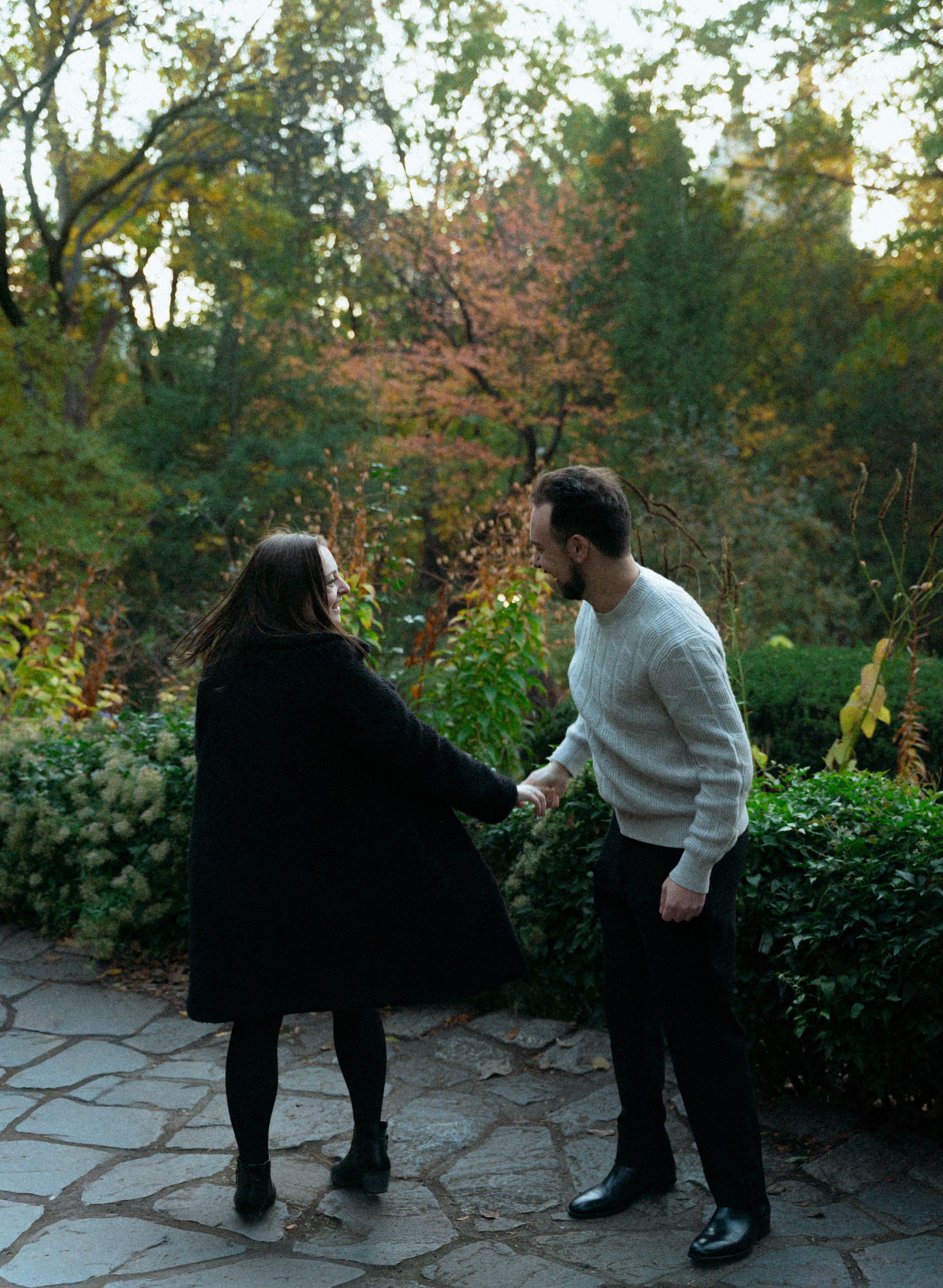 Two people dancing playfully on stone patio surrounded by autumn foliage.
