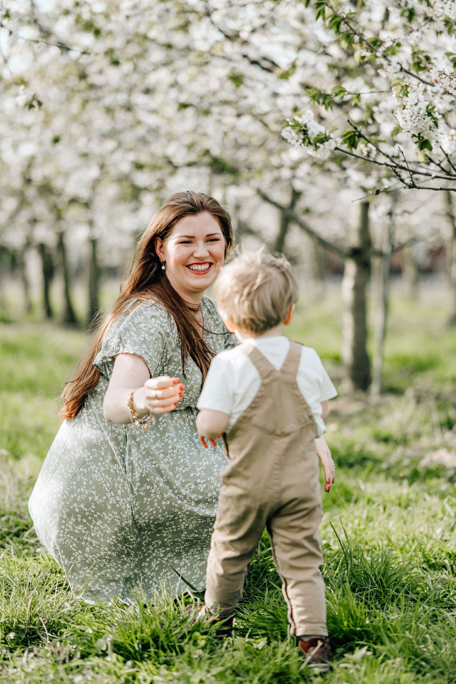 A joyful moment captured in a blooming spring cherry orchard with white blossoms and green grass.