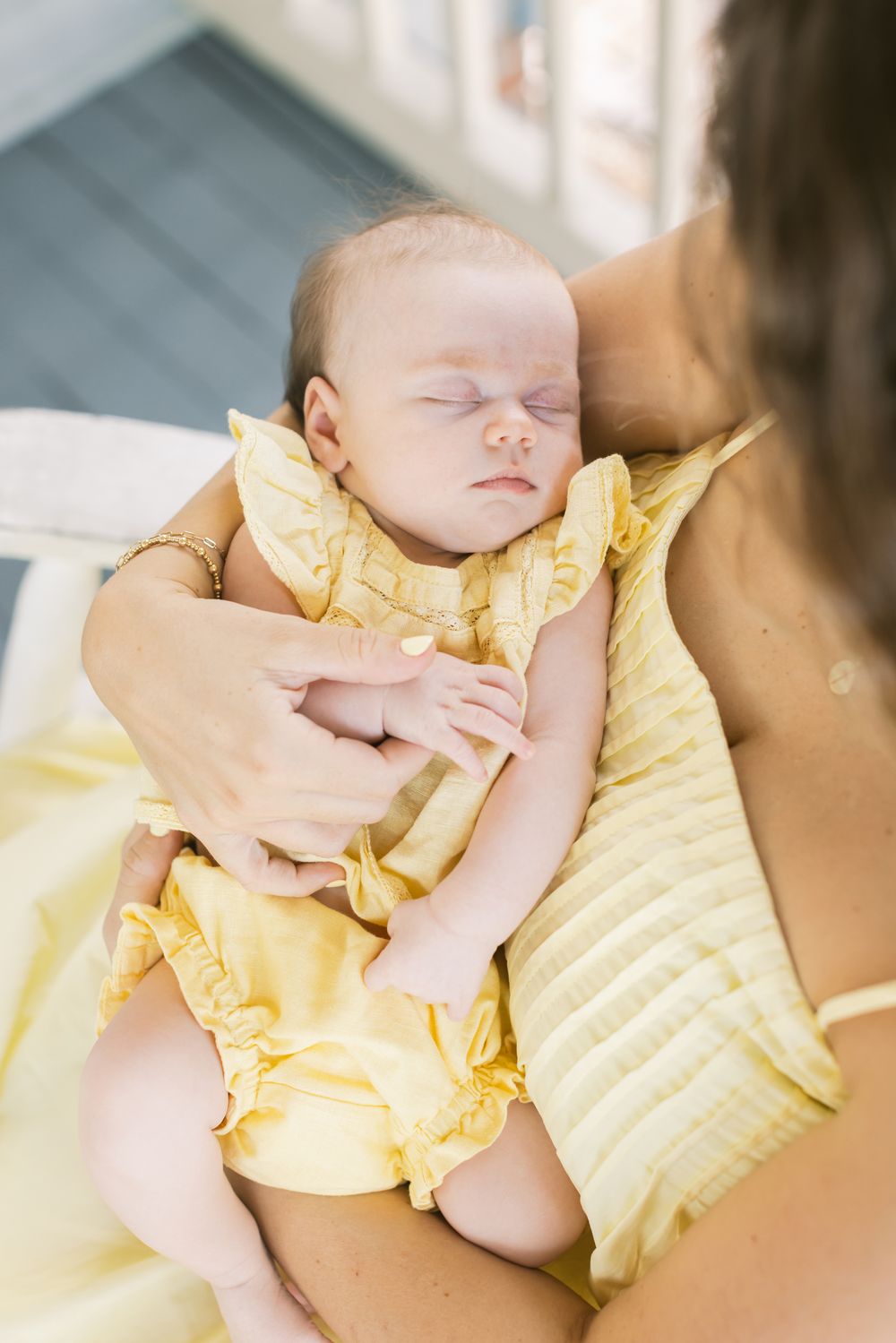 A sleeping newborn wearing a pale yellow dress matching and being held by her mother of newborn photos. Concord MA NH newborn photographer.