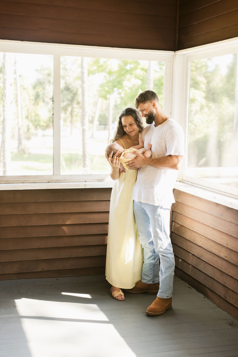 A couple gazes at their newborn girl on a screened in porch for newborn photos. Lakes Region, Meredith, Laconia newborn photographer.