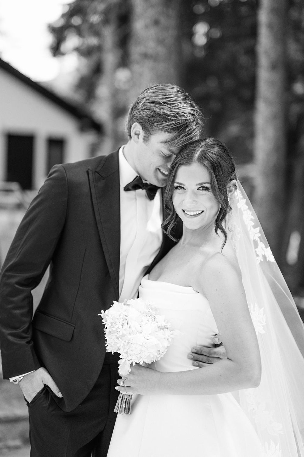 Black and white romantic wedding photos showing tender moments between bride in white dress and groom in dark suit.
