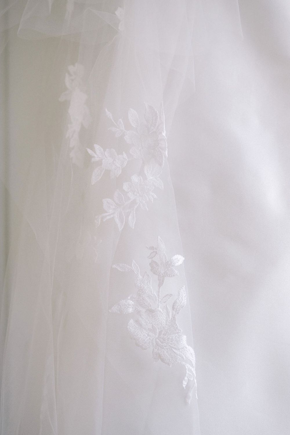 Delicate white lace veil with floral embroidery details in soft lighting.