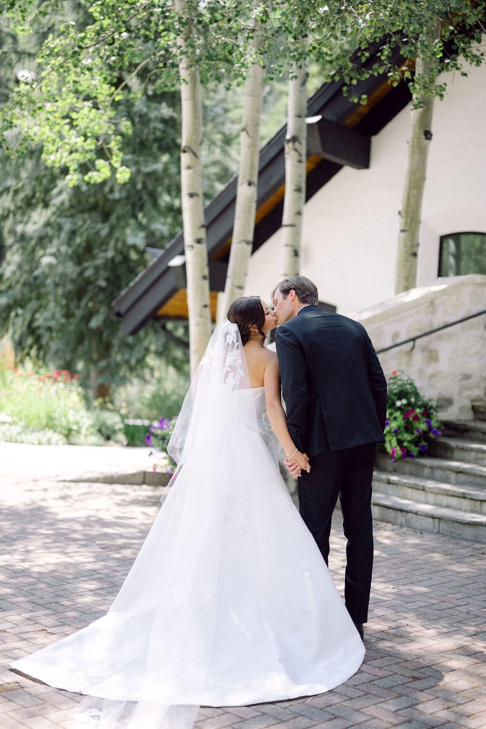 A romantic wedding couple shares an intimate moment on stone steps with aspen trees in the background.