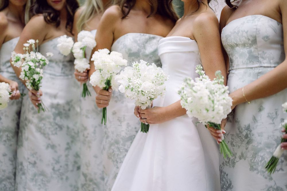 Bridesmaids in gray dresses hold elegant white floral bouquets during a wedding ceremony.