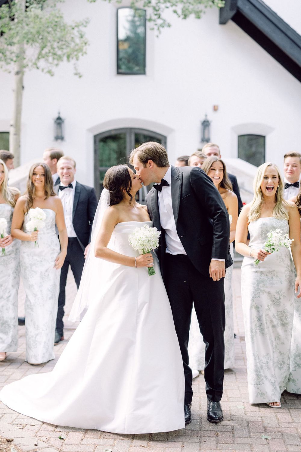 Wedding party poses together outside a white building with bridesmaids in elegant dresses.