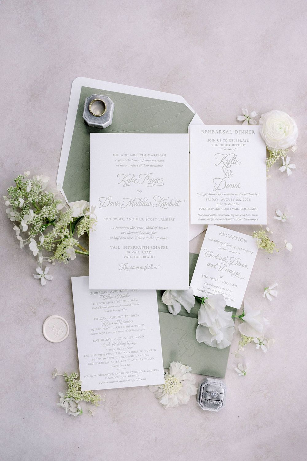 Elegant white wedding invitation suite with delicate floral details arranged on light gray textured background.