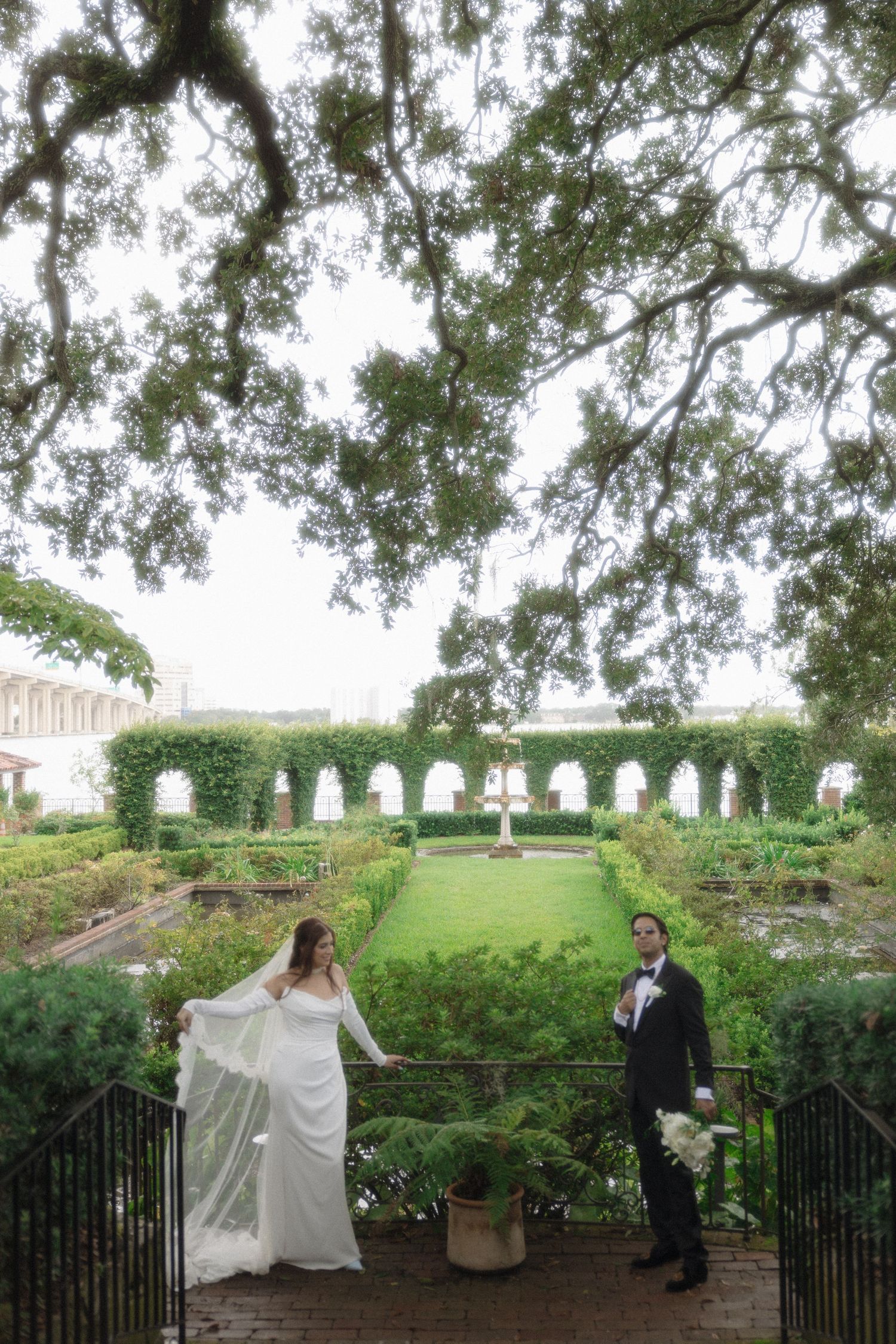 A black and white photo series showing a couple walking along a stone wall with trees and headstones in the background.