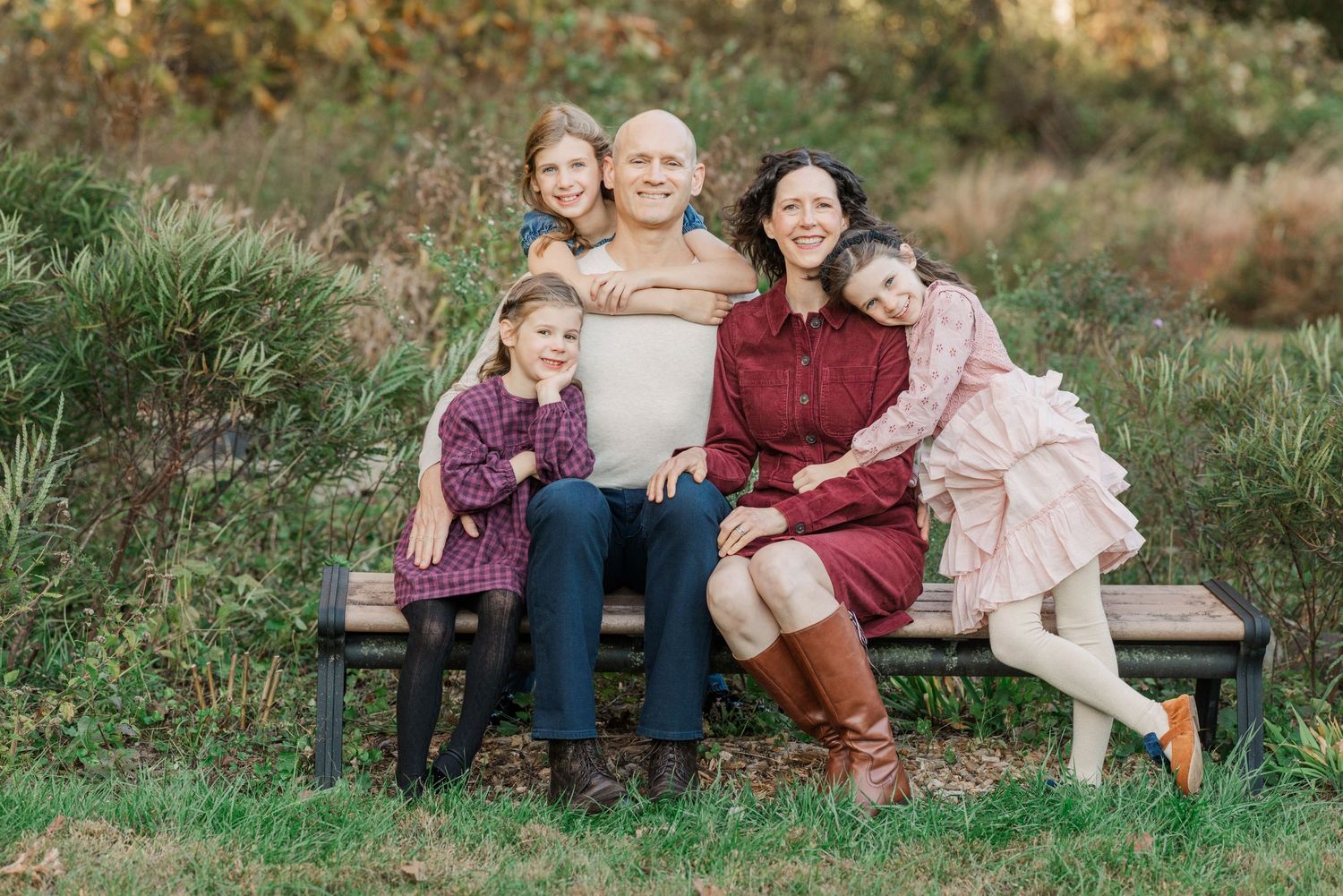 A family sits together on a wooden bench outdoors in a grassy field during golden hour.