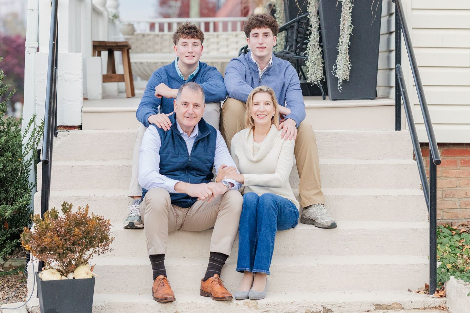 A couple sits casually together on white porch steps during an outdoor photo session.