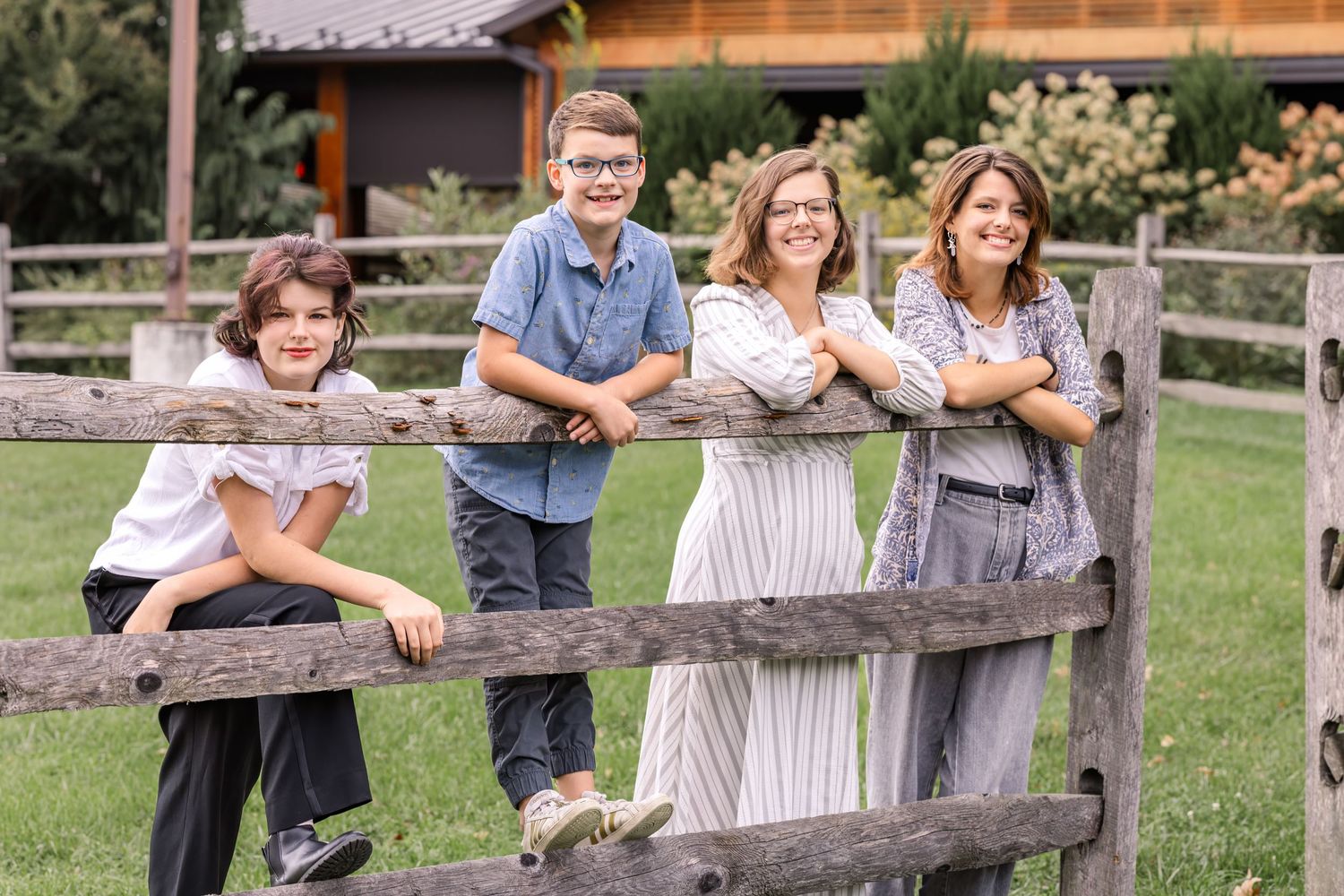 Family members lean against a rustic wooden fence while posing together outdoors in a grassy field.
