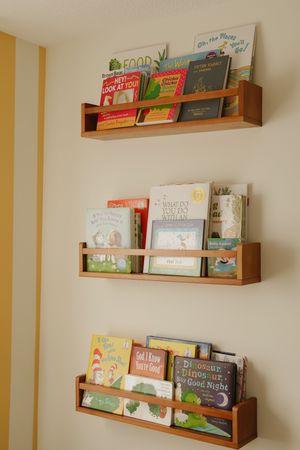 Modern nursery with wooden floating shelves displaying children's books.