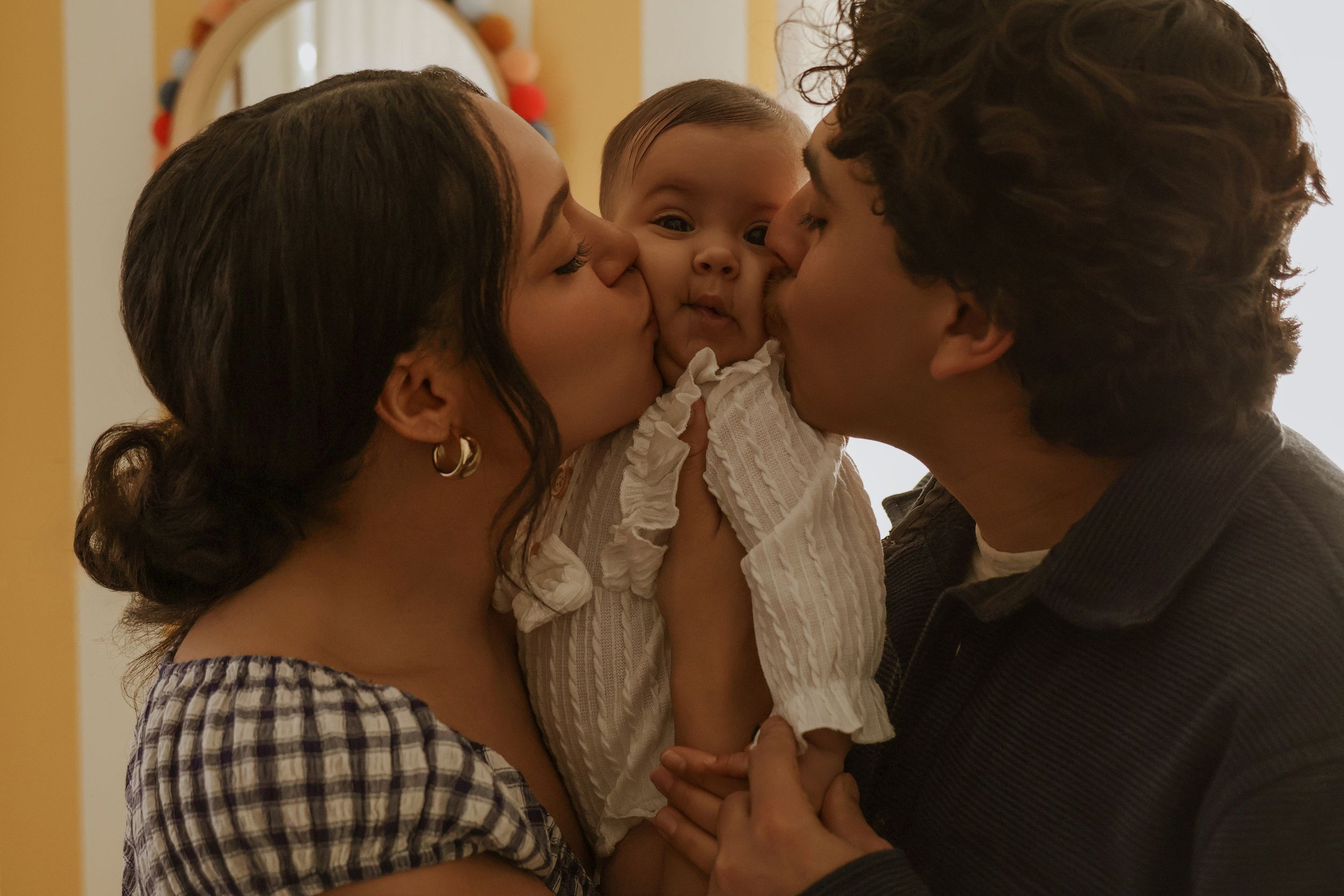 Tender family moment captured in warm lighting against striped wall.