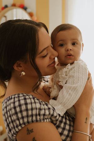 Parent and baby share affectionate moment in front of striped wall with warm lighting.