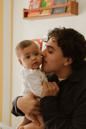 Parent and baby sharing sweet kisses in nursery with bookshelves.