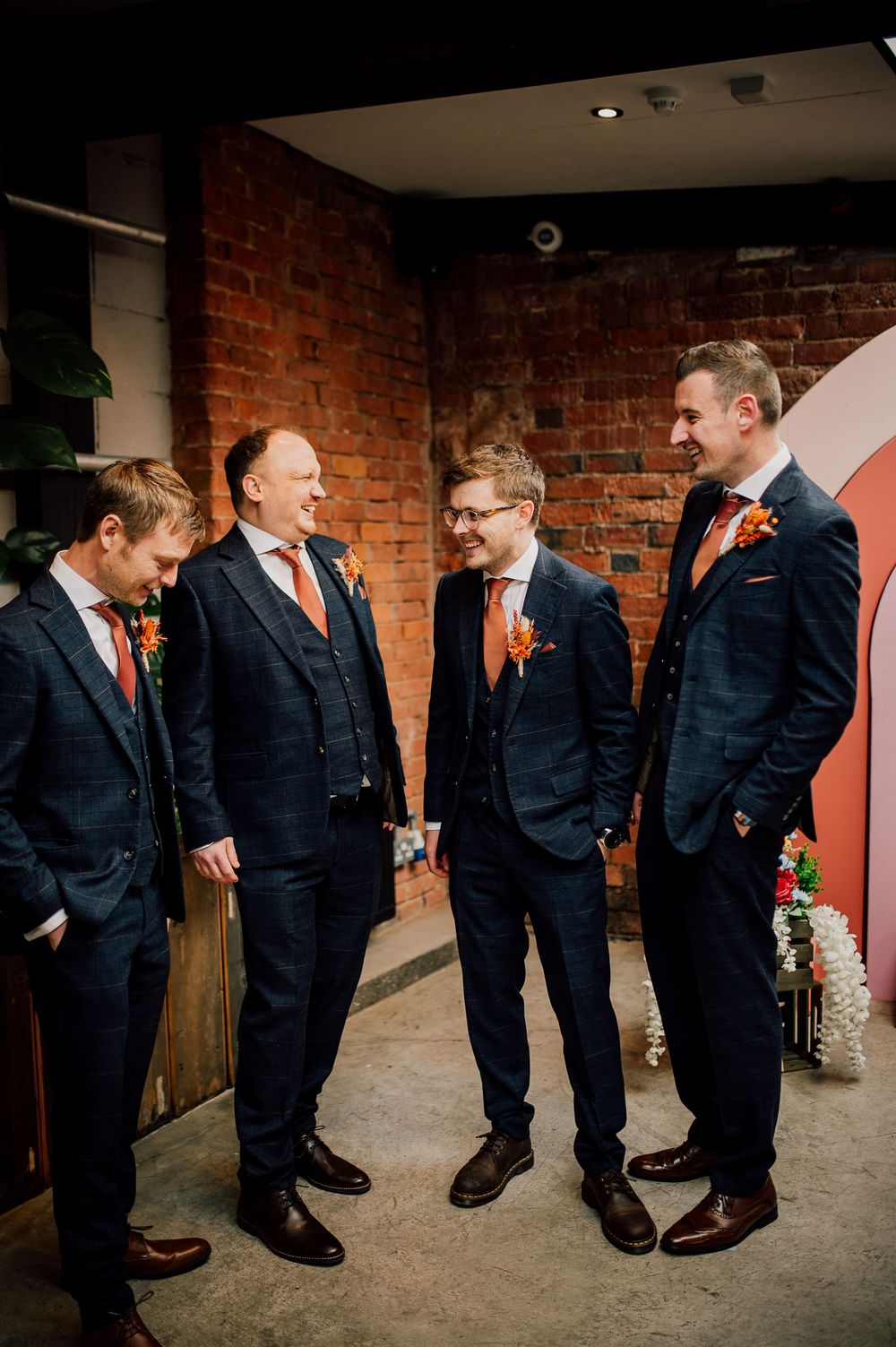 Wedding party members in dark suits gather in a sequence of candid moments showing casual interactions and laughter.