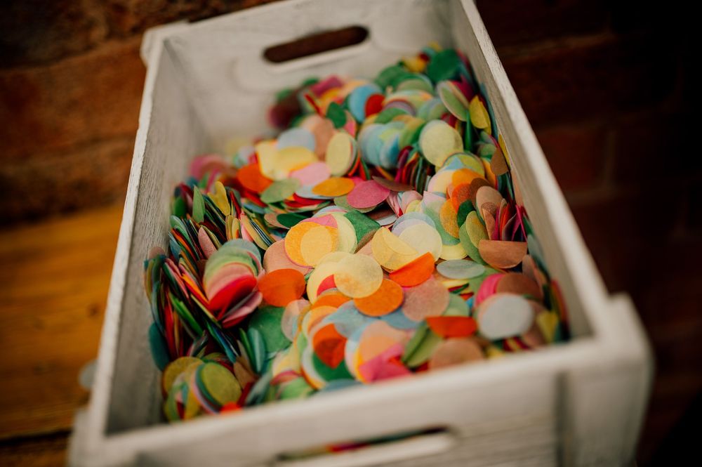 A white wooden box filled with colorful round confetti or paper dots in various pastel and bright shades.