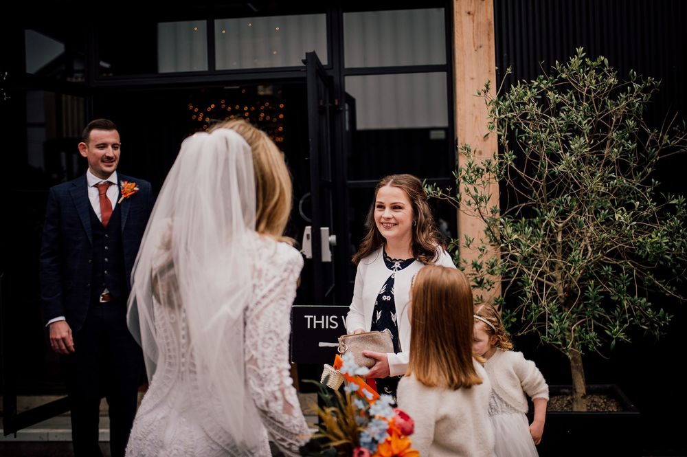 Wedding guests gather outside a venue entrance with a small child holding a pumpkin for fall festivities.