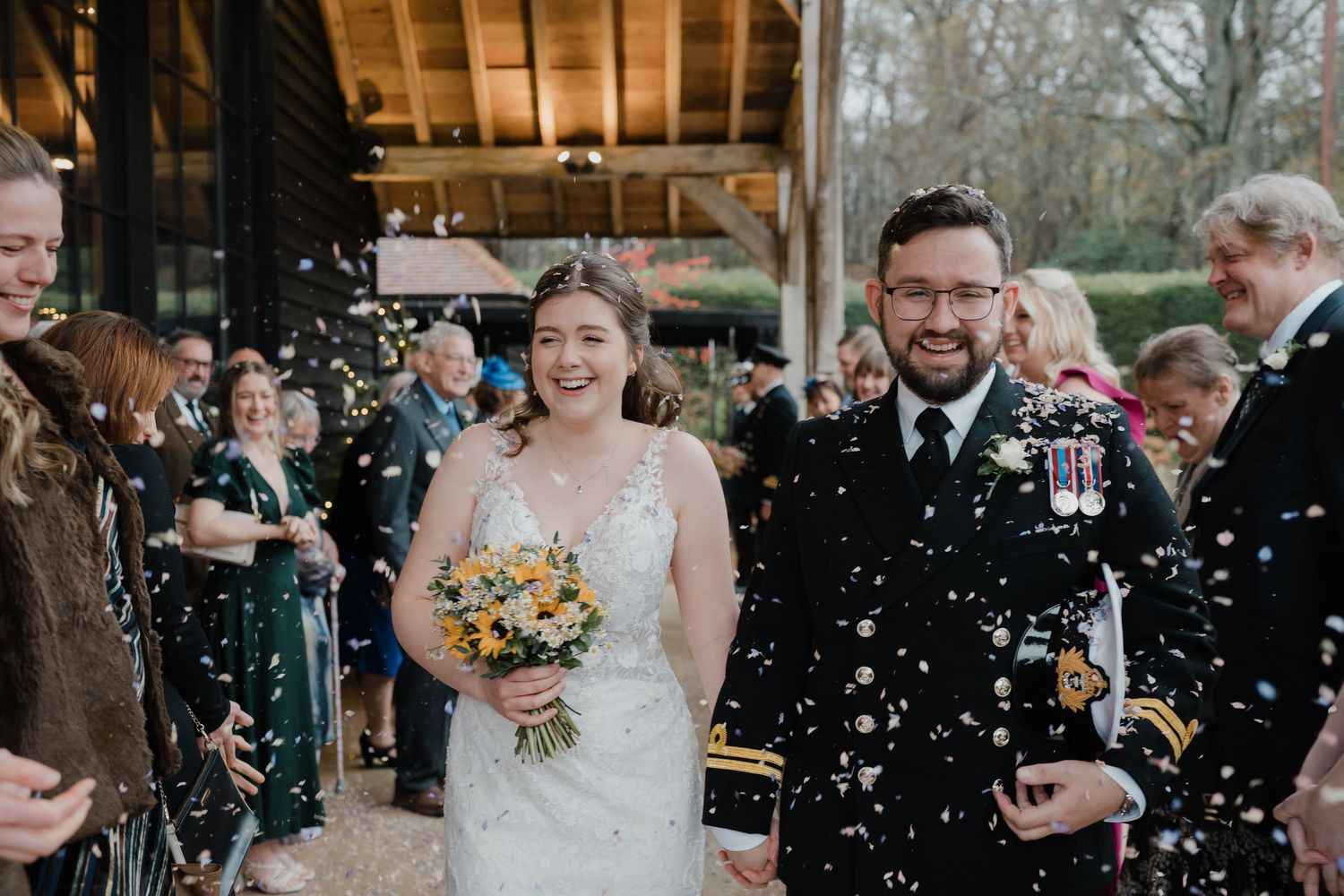Happy couple walks through shower of confetti after their wedding ceremony at rustic outdoor venue.