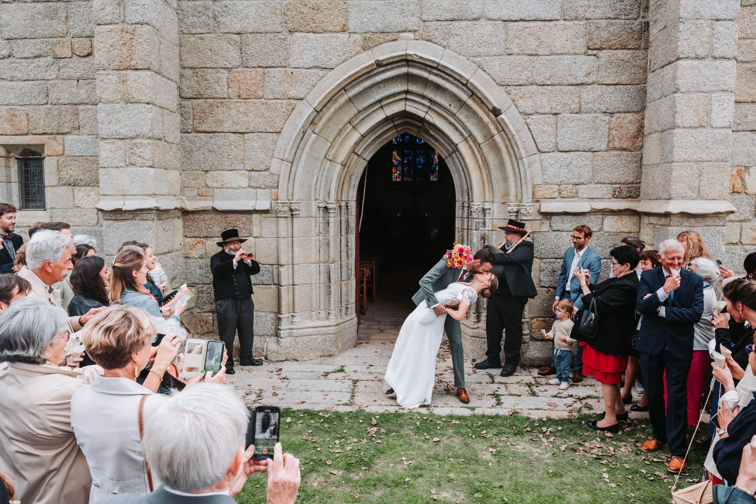 Sortie de cérémonie devant une église en pierre en Bretagne, mariés accueillis par leurs invités.
