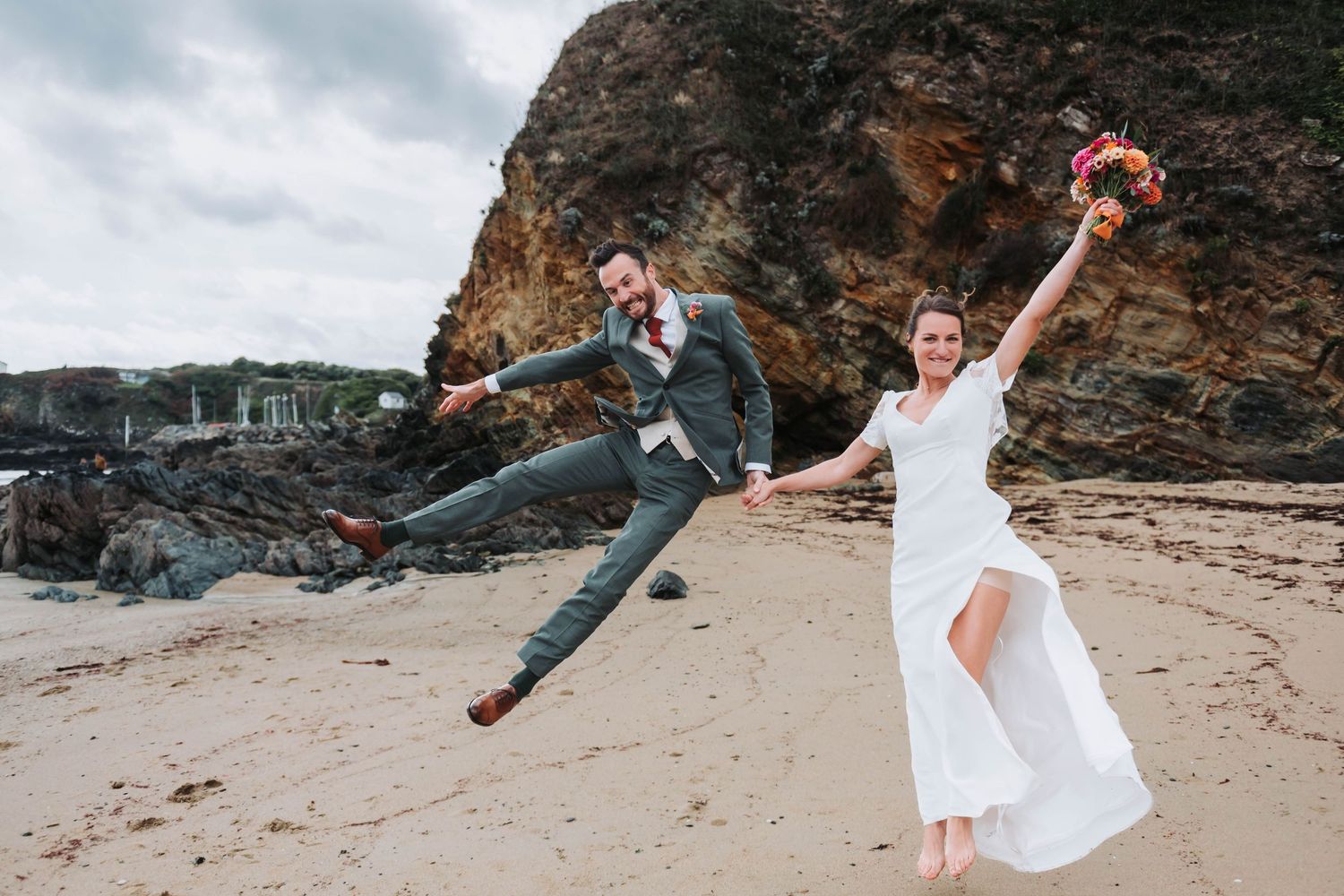 Mariés sautant et riant sur une plage bretonne, séance photo couple naturelle et vivante.