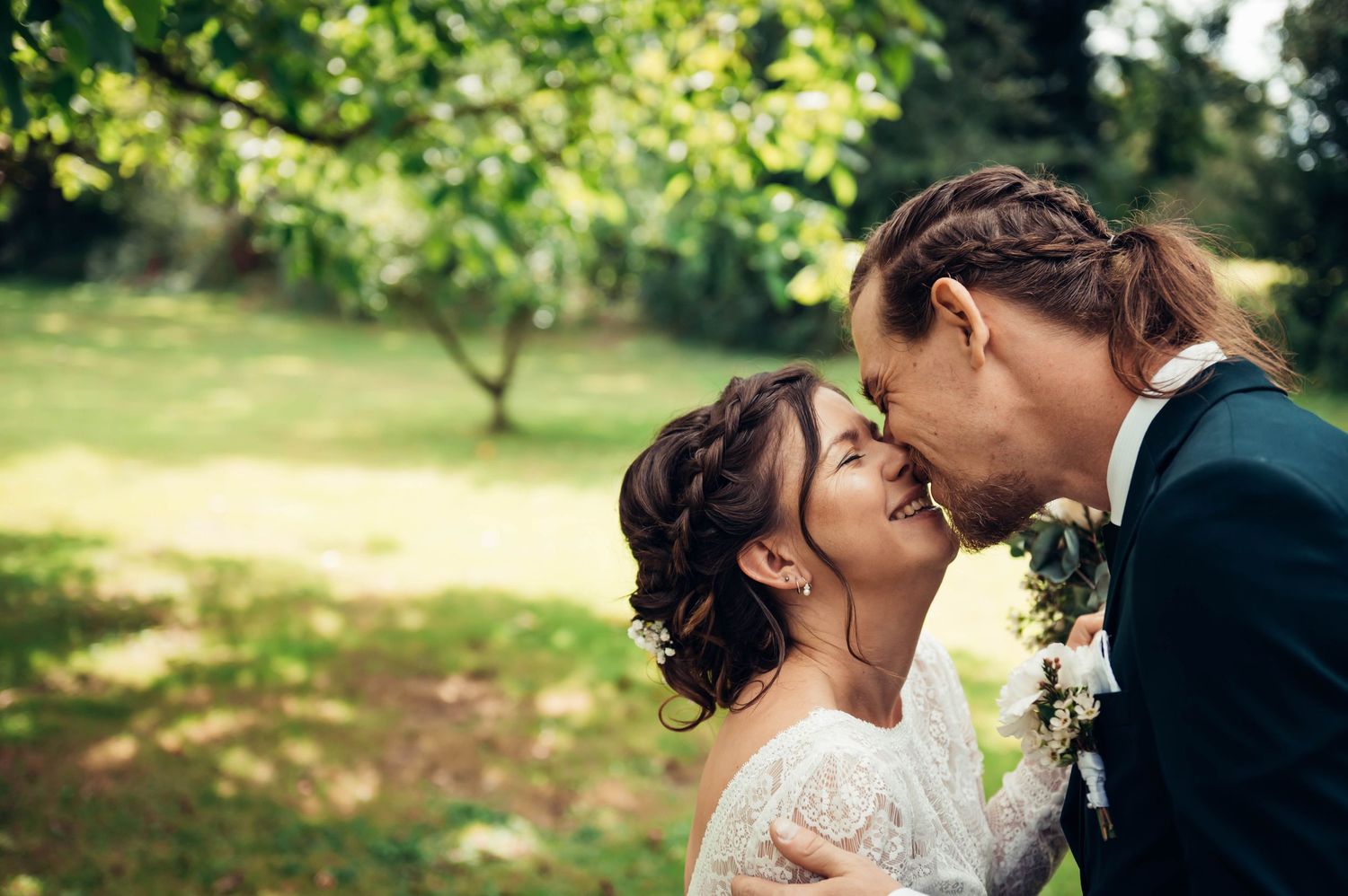 Couple de mariés s’embrassant dans un jardin ensoleillé en Bretagne, photo de mariage naturelle.