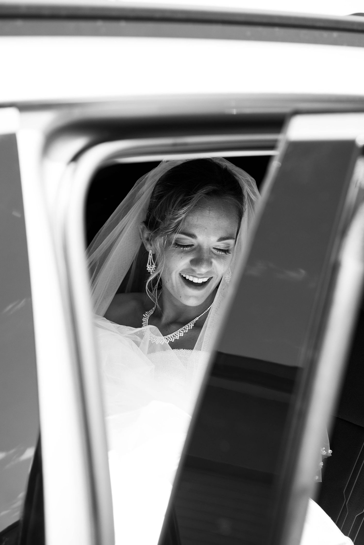 Mariée souriante à travers la fenêtre d’une voiture le jour de son mariage en Bretagne.