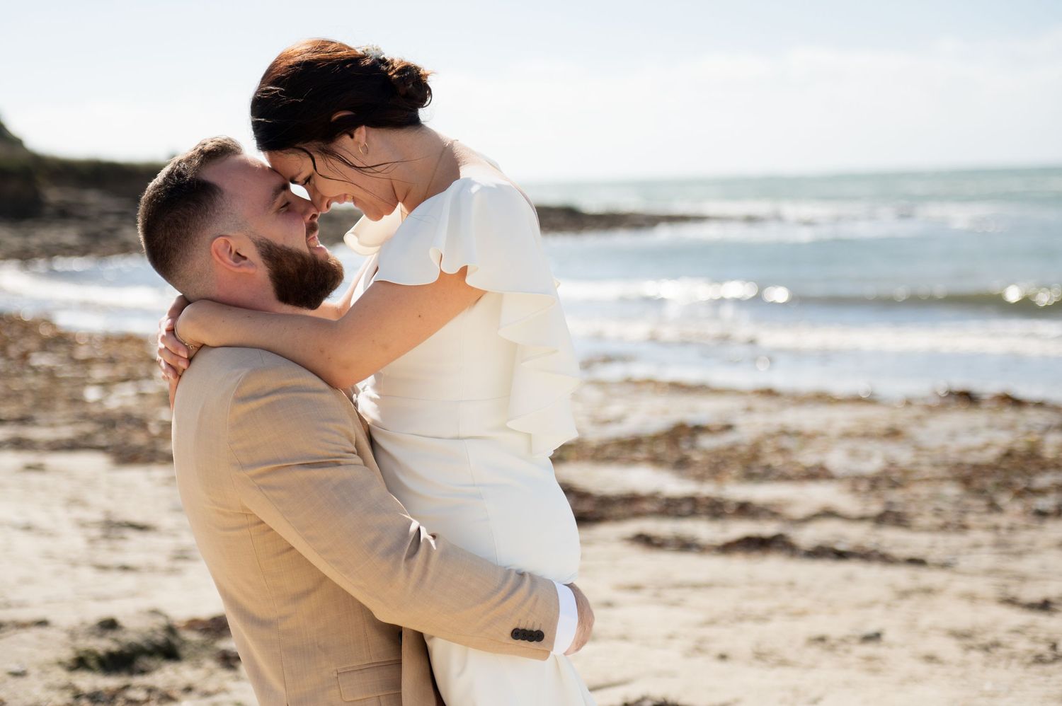 Couple de mariés enlacé sur une plage en Bretagne avec l’océan en arrière-plan, séance photo mariage bord de mer.