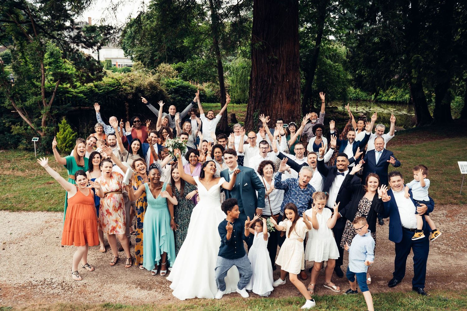 Grande photo de groupe en extérieur, invités levant les bras dans une ambiance festive lors d’un mariage en Bretagne.