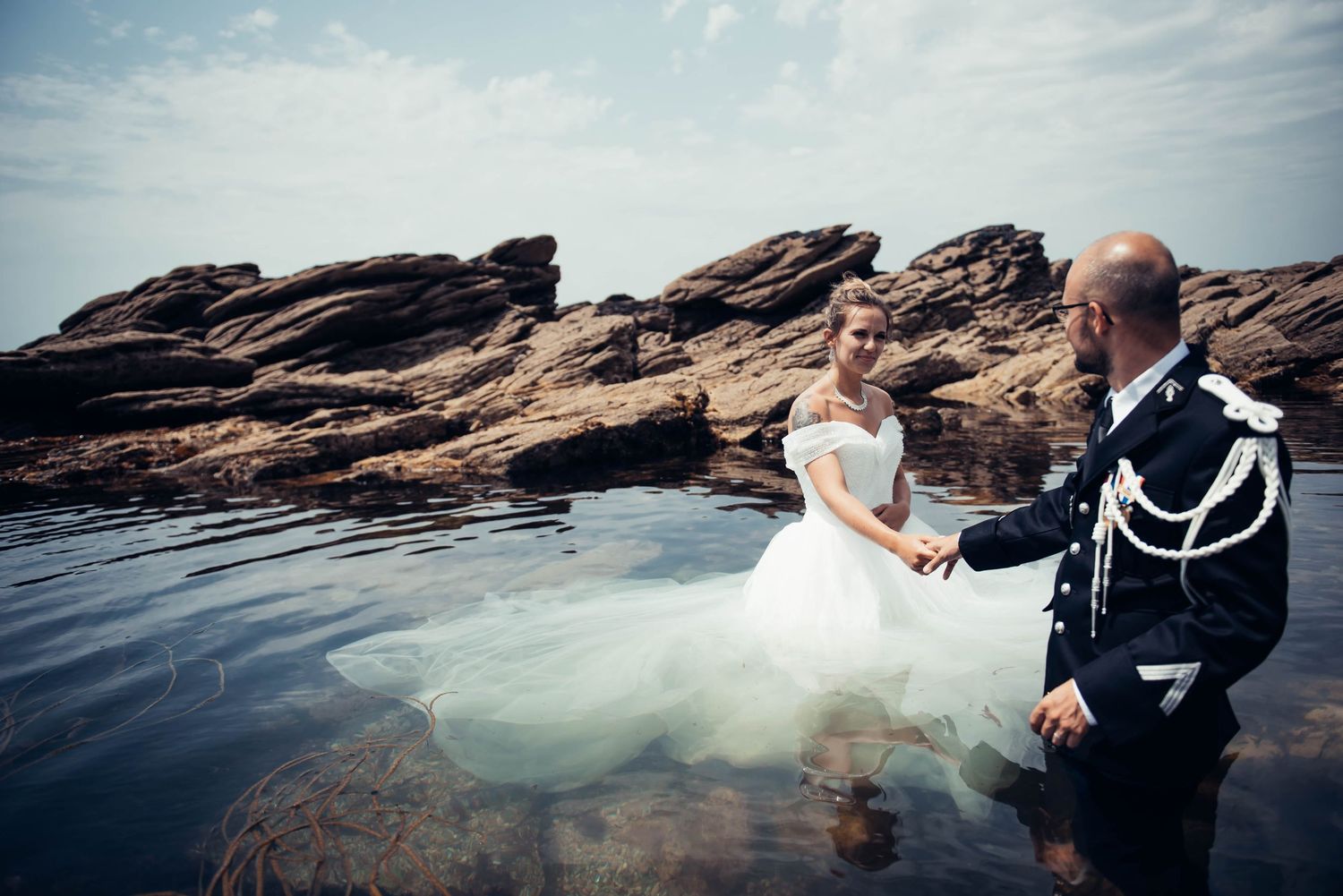 Couple de mariés photographié sur des rochers face à l’océan en Bretagne, séance photo mariage bord de mer.