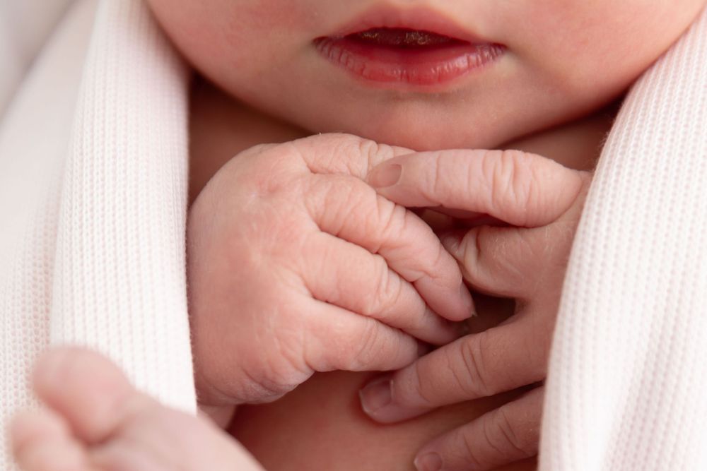 Close up view of a baby's tiny fingers grasping a soft white fabric.