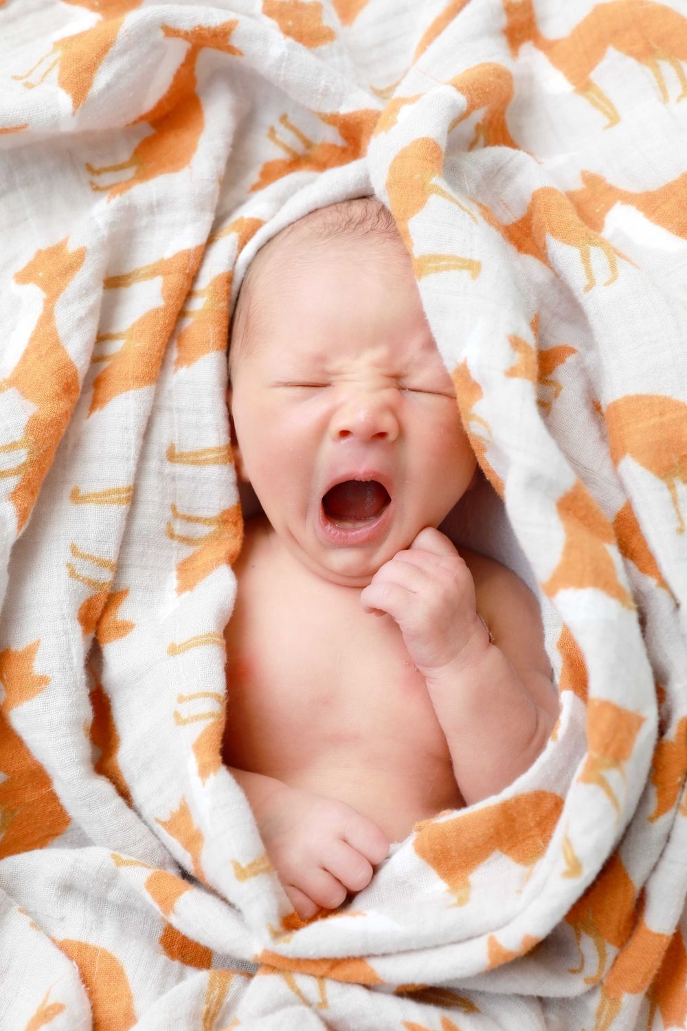Happy baby wrapped in orange and white patterned blanket smiles while laying down.