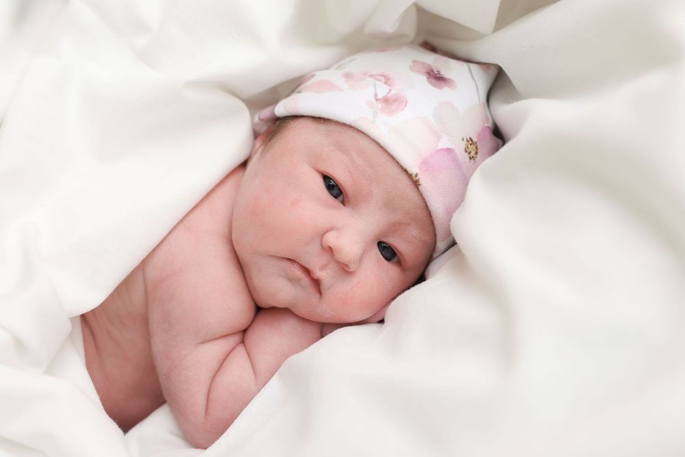 Newborn baby wrapped in soft white blanket sleeping peacefully with rosy cheeks.