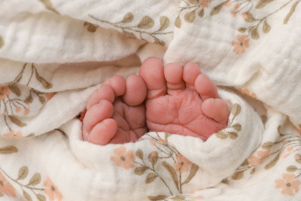 Tiny newborn baby feet resting on a floral patterned blanket.