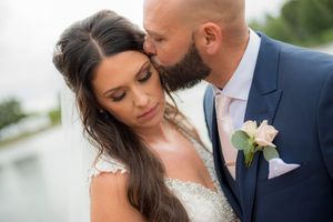 Groom in navy suit kisses bride on forehead during romantic outdoor wedding portrait.